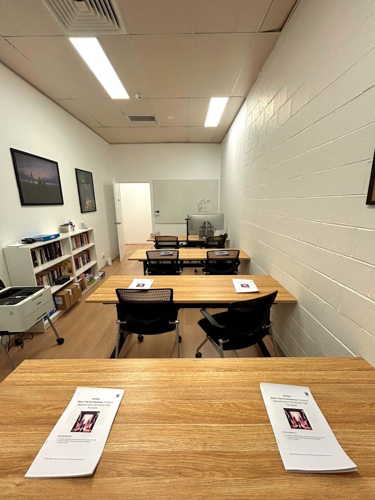 Classroom with rows of timber desks set with Gilgamesh and Odyssey handouts, a bookshelf and a whiteboard