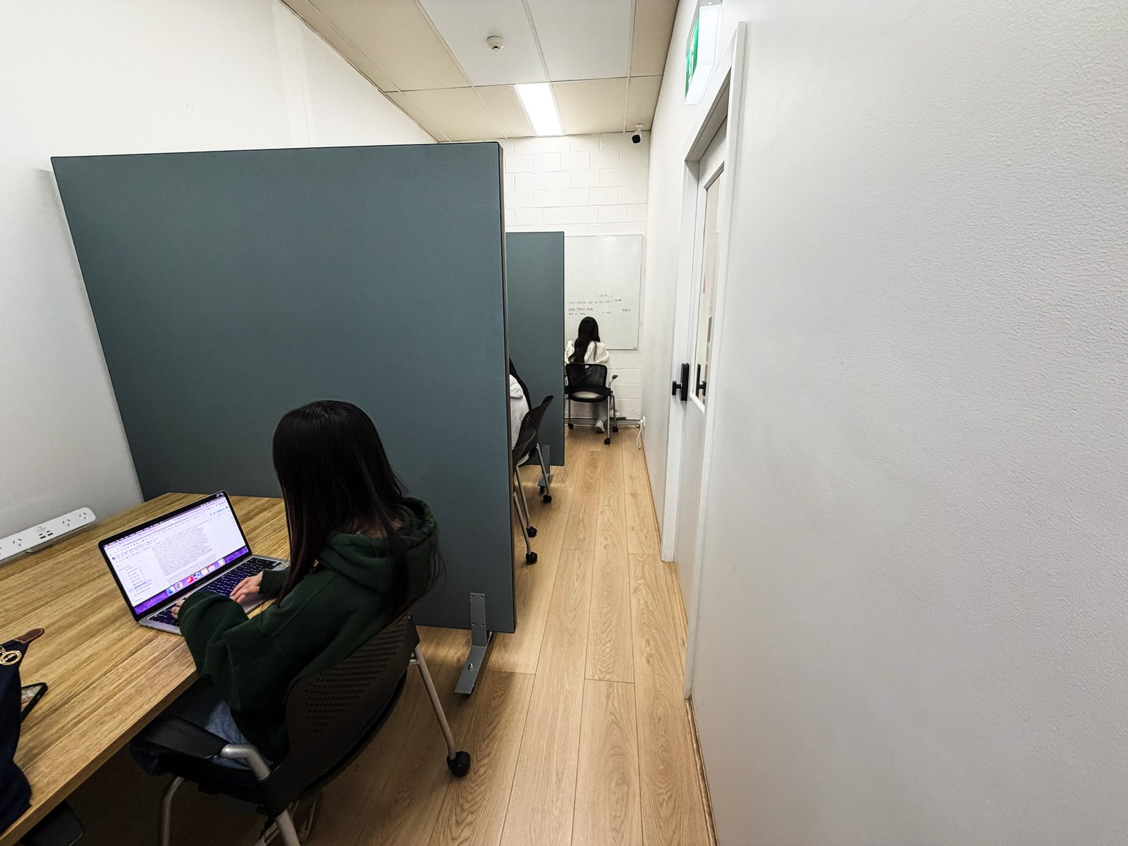 Students working at laptops in quiet study booths, seen from behind